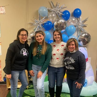 Four women smile in front of a balloon and silver star display, with an inflatable polar bear on the right.