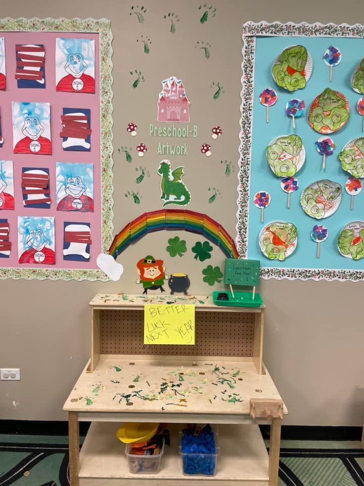 Classroom display featuring art projects, a rainbow with a leprechaun, and a wooden table with supplies for children.