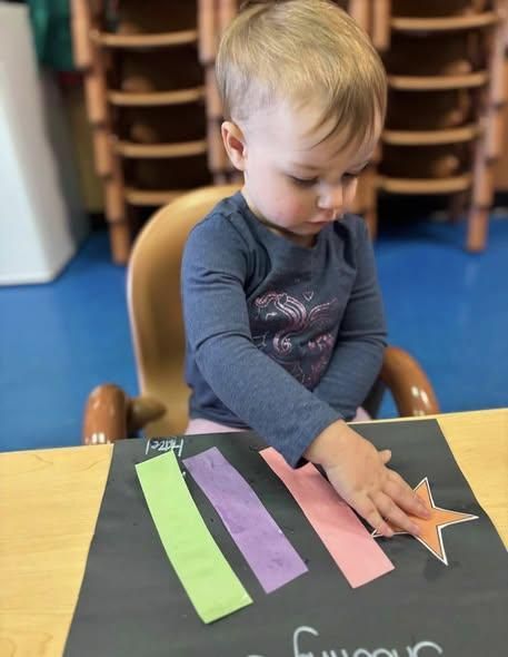 A person focuses on placing a paper star onto a black construction paper sheet.