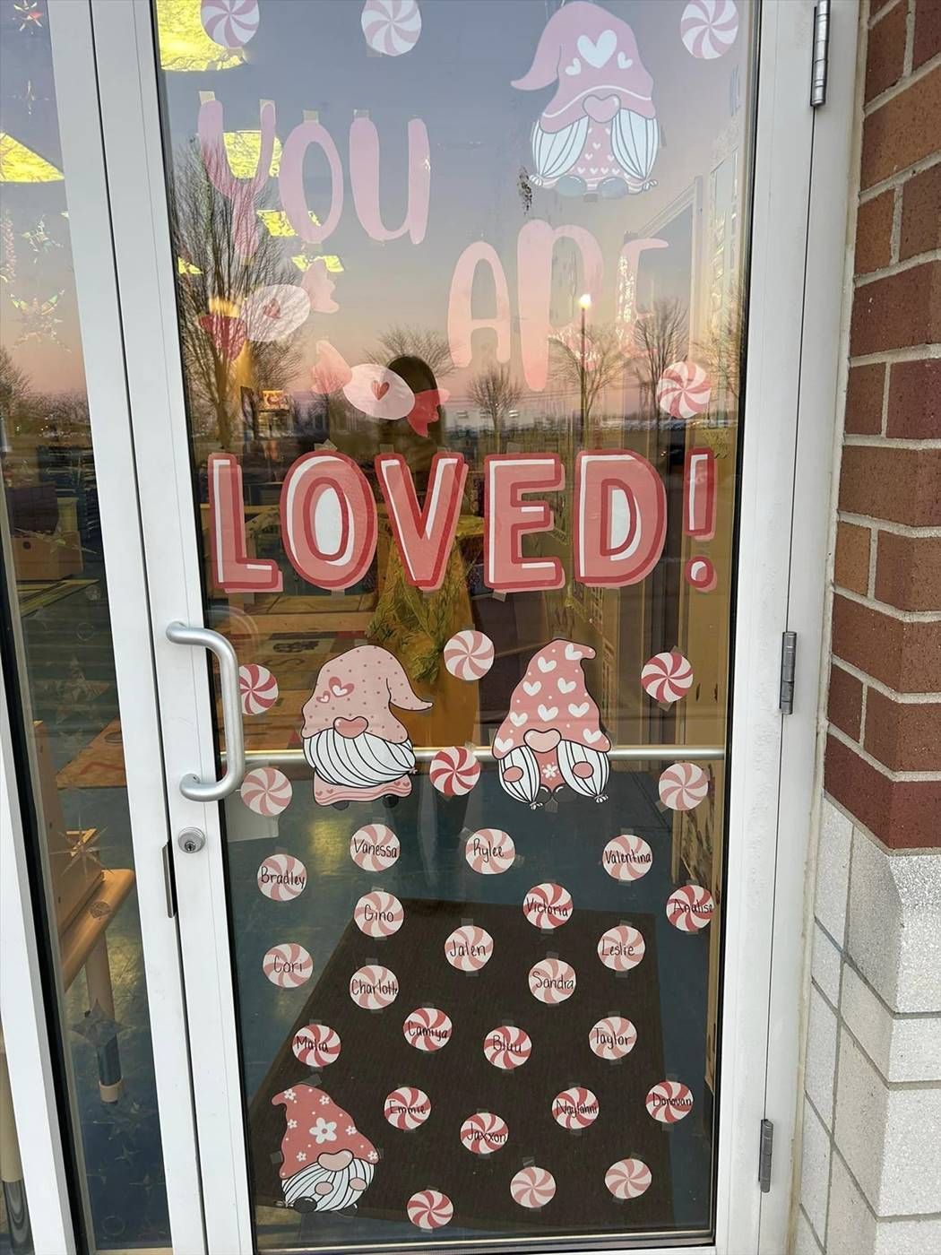 A glass door decorated with pink and white gnome stickers, peppermint candies, and the text 