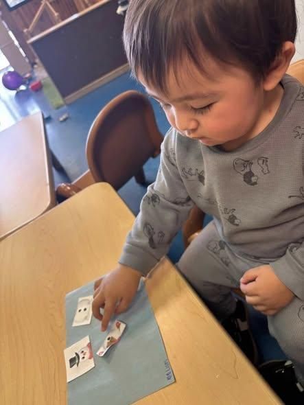 A child sitting at a table uses their finger to point to small printed cards on a blue sheet of paper.