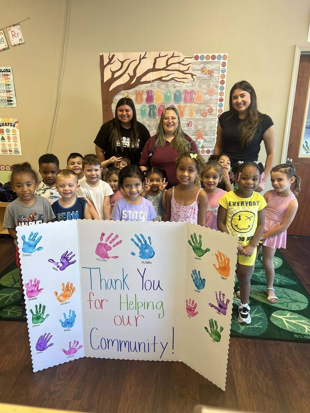 A group of children and adults smile behind a sign that reads, 