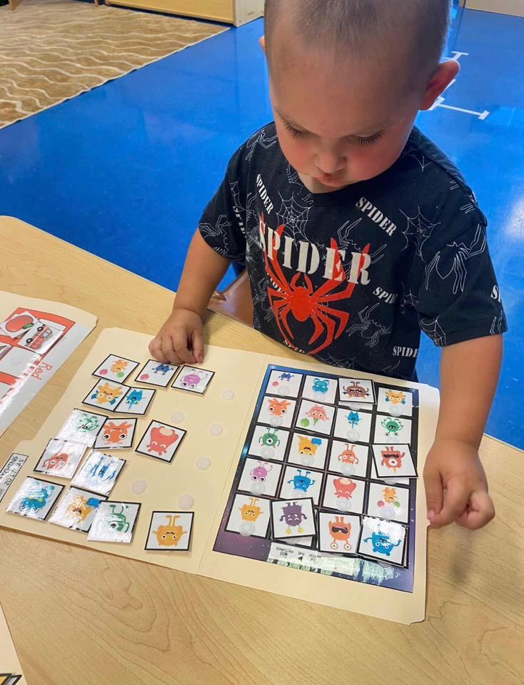 A child engaged in a matching activity, placing small square cards onto a matching grid on a manila folder on a table.
