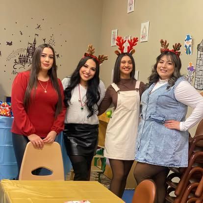 Four people wearing festive reindeer headbands stand together indoors in a cheerful, decorated room.