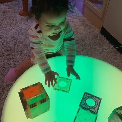 A person playing with translucent magnetic tiles on a circular, glowing green light table.