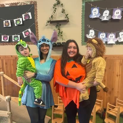 Two adults in costumes hold two children in animal onesies in front of a wall with holiday decorations.
