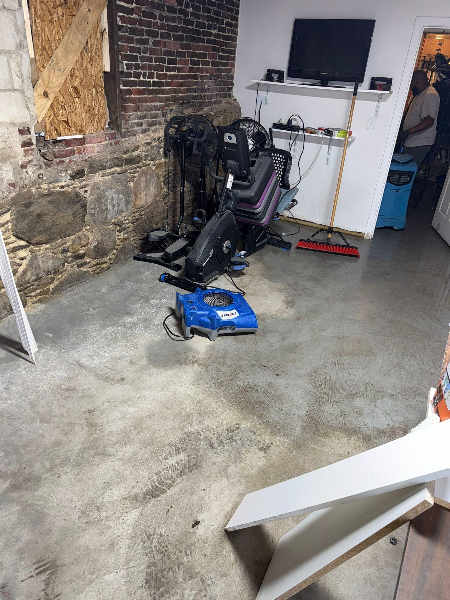 Basement/workshop with a black recliner chair and blue tool case on a concrete floor near shelves and a brick wall