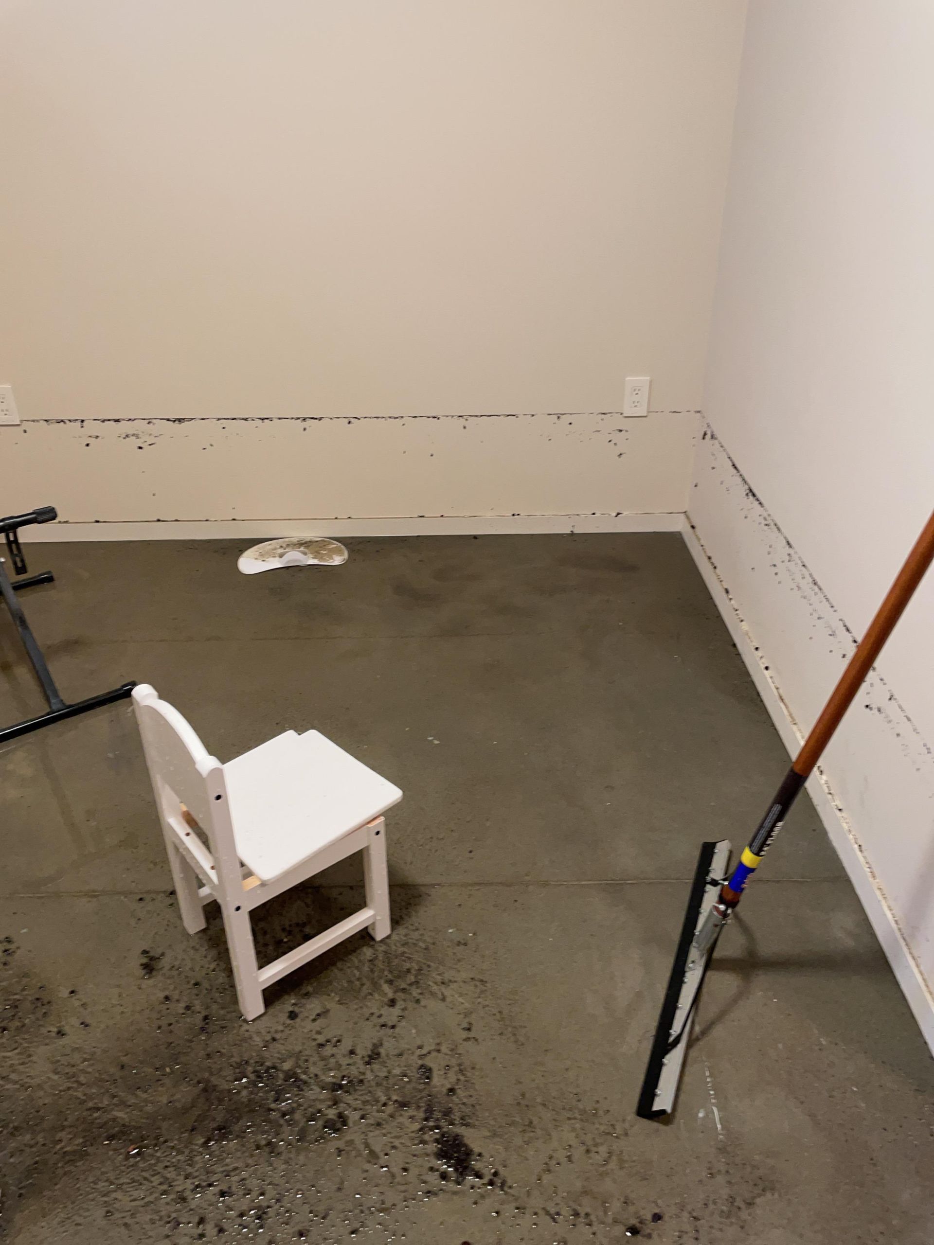Empty room with gray floor, white chair, and a mop leaning against the wall