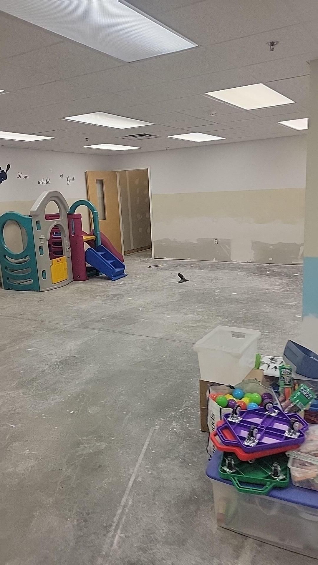 Empty room under renovation with bare floors, ceiling lights, and stacked toys and play equipment.