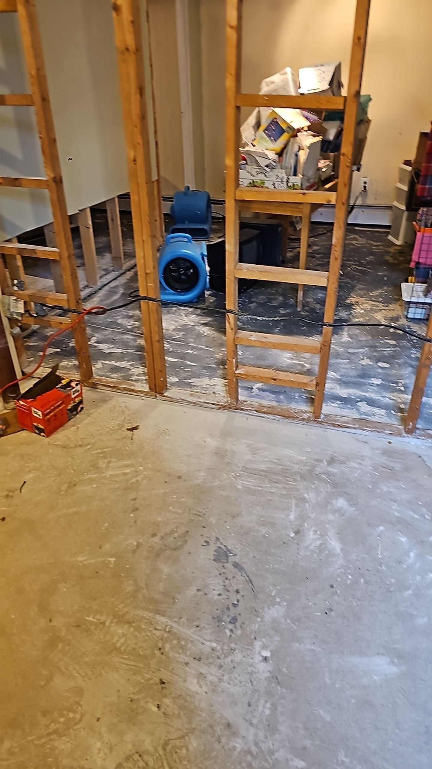 Partially demolished room with exposed studs, debris on the floor, and a blue fan near the wall