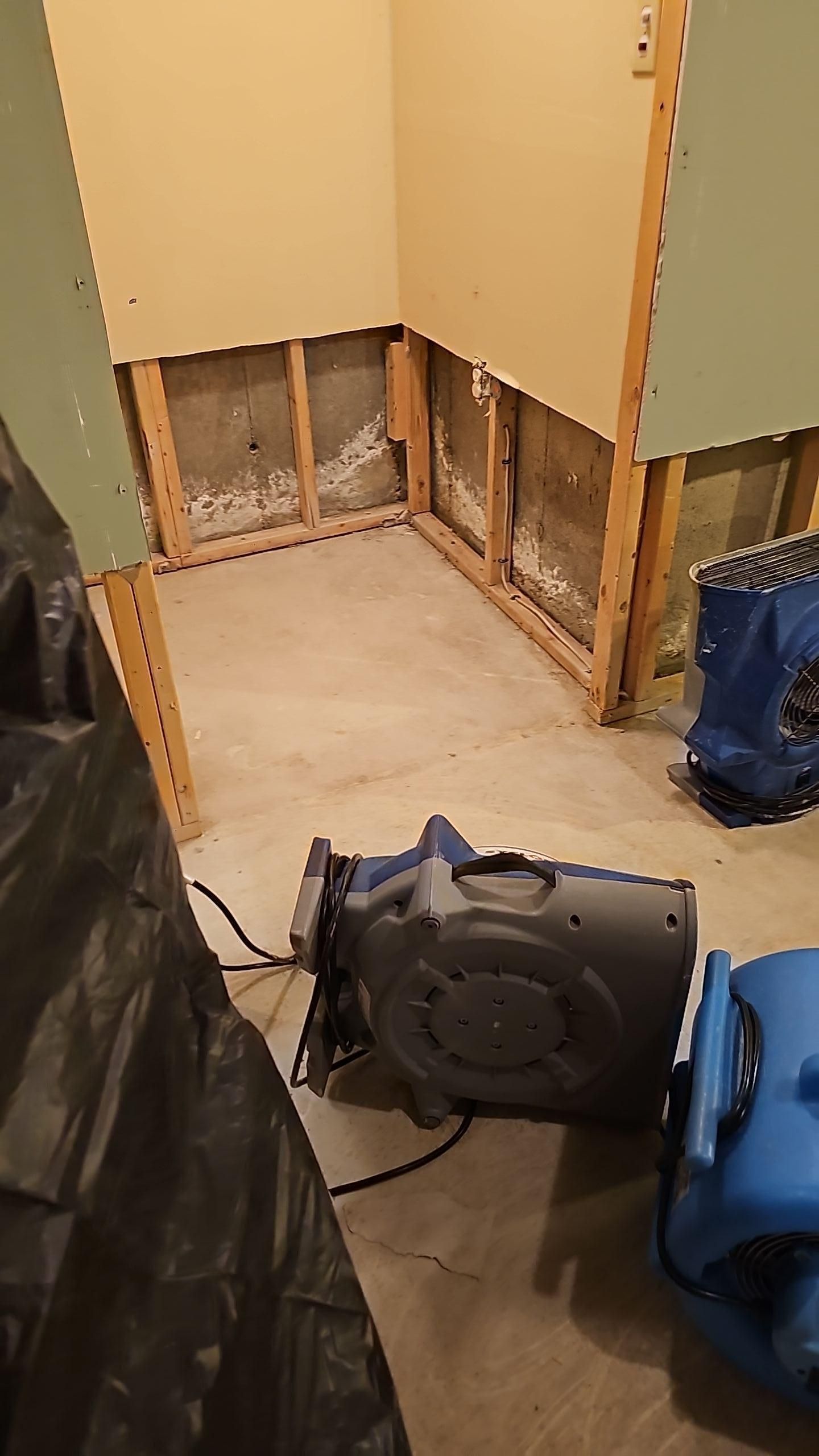 Unfinished room with exposed wall studs, a blue fan, and construction materials on the floor.