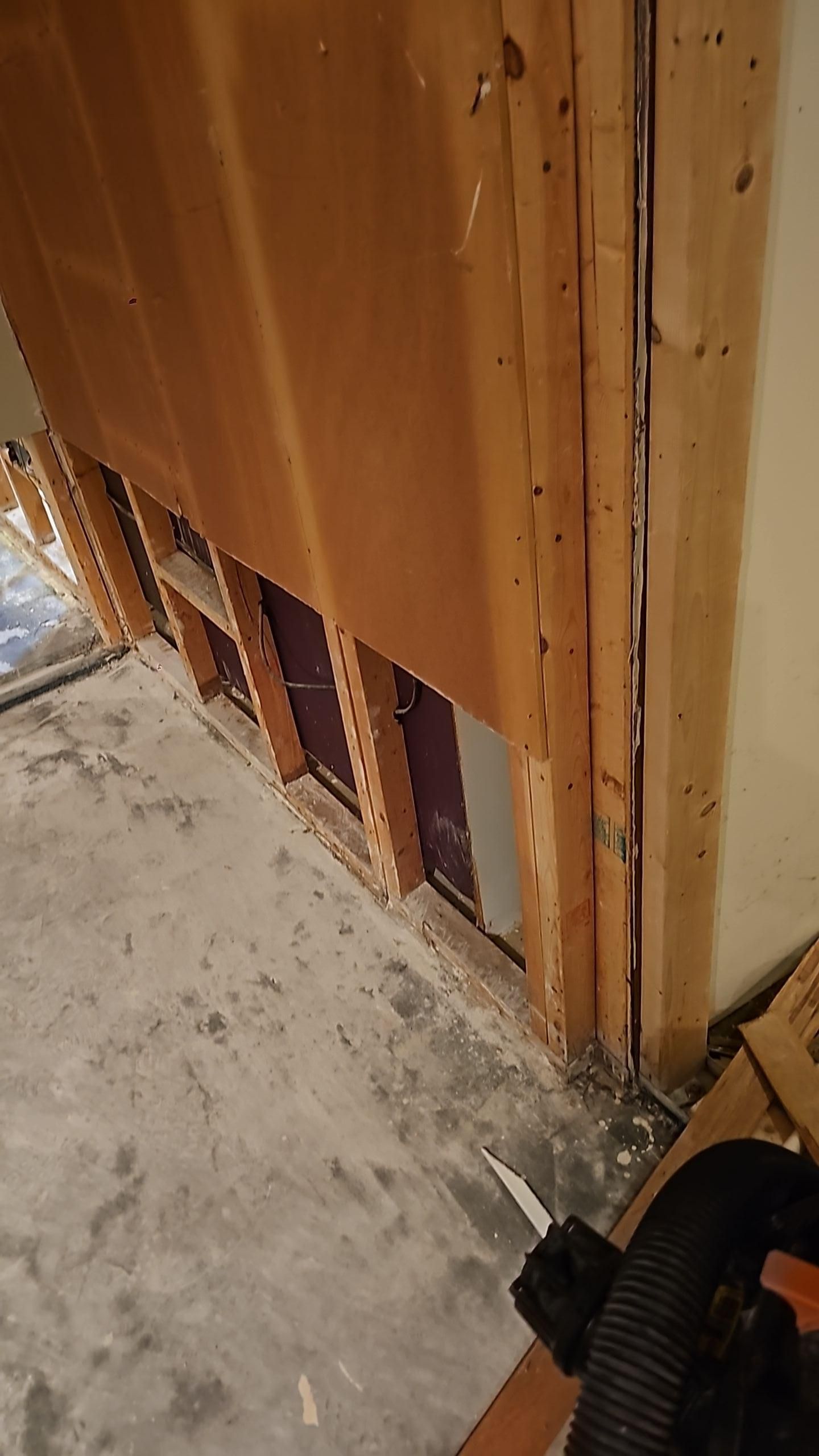 Damaged wooden wall or cabinet with exposed studs and debris on a concrete floor