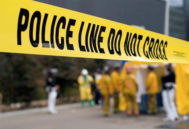 Police line do not cross tape cordoning off a blurred scene with responders in yellow suits
