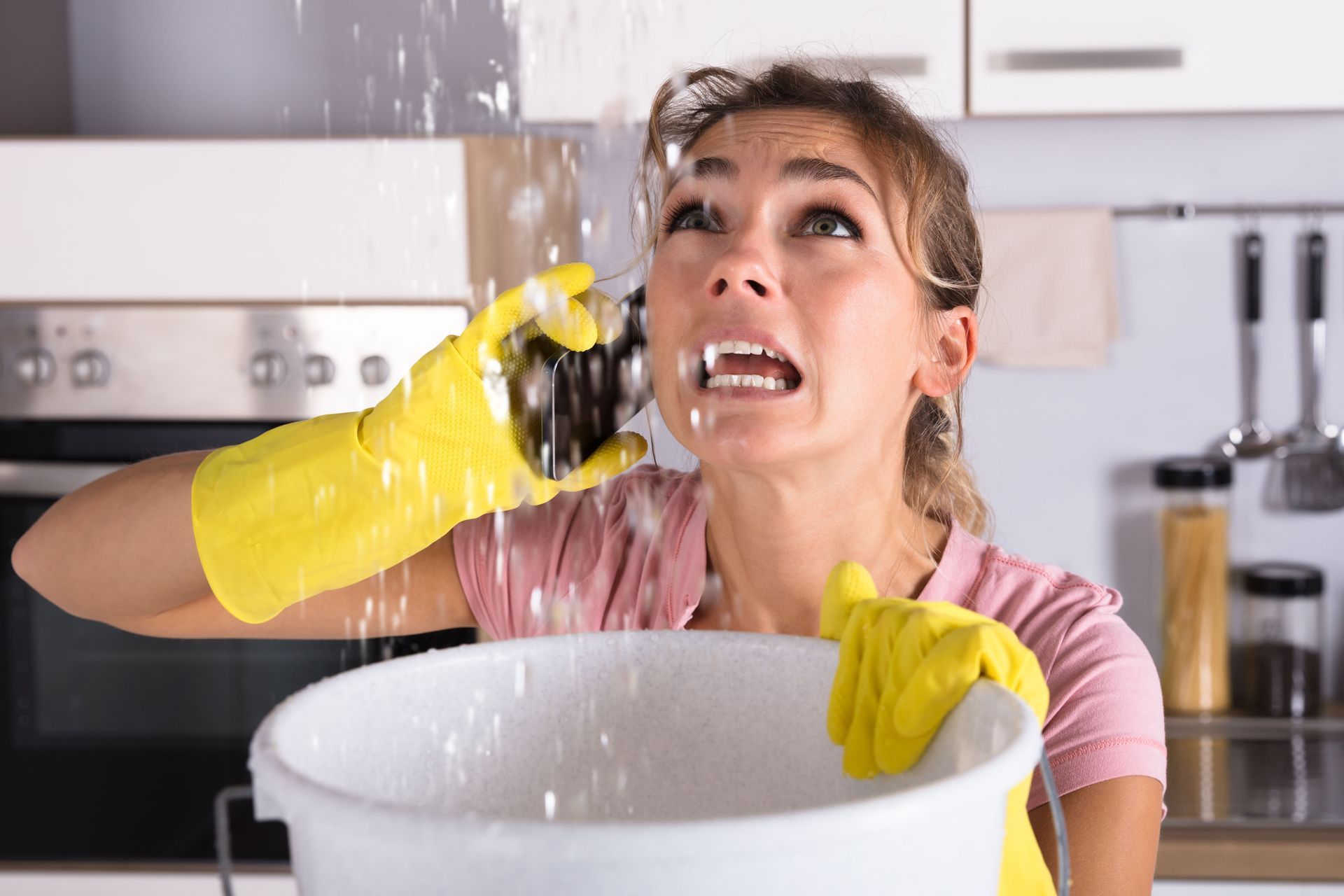 Woman in yellow gloves splashing water while washing dishes in a kitchen, looking startled