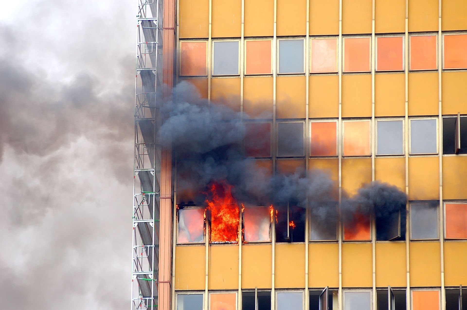 High-rise building windows engulfed in flames with thick black smoke billowing बाहर