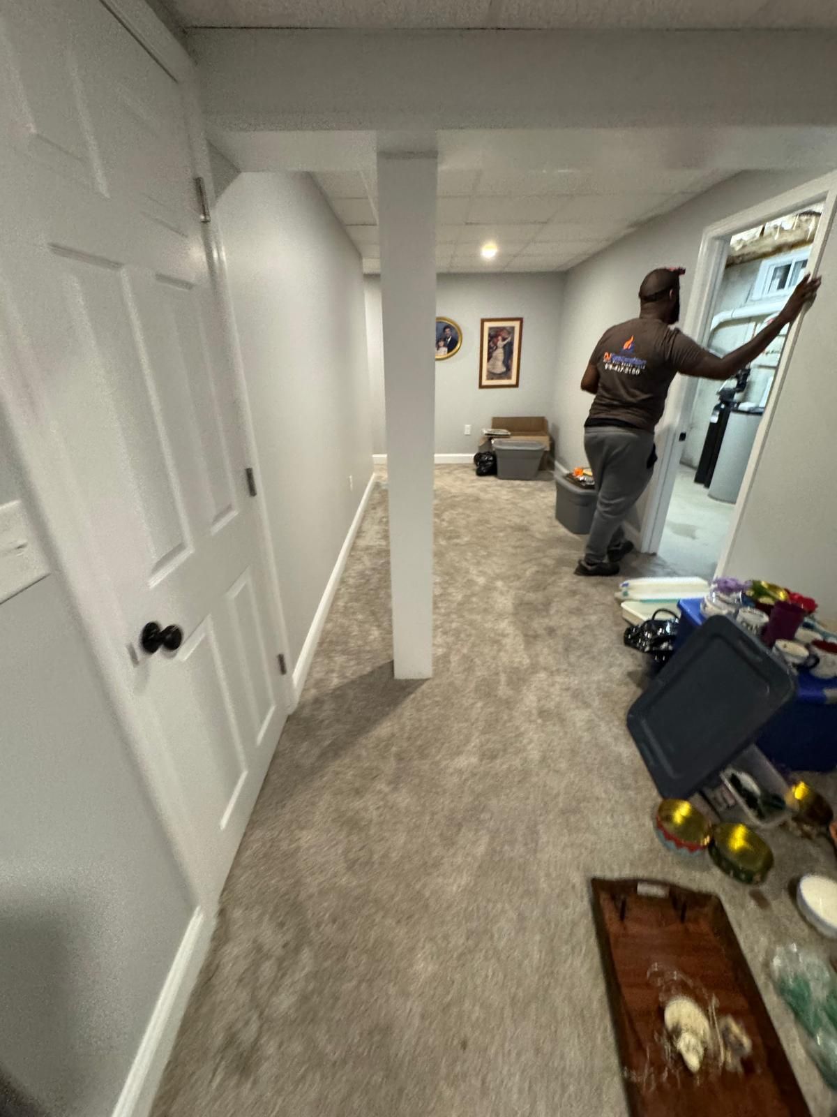 Hallway with carpet and open closet; man in gray shirt reaches for a framed wall piece.