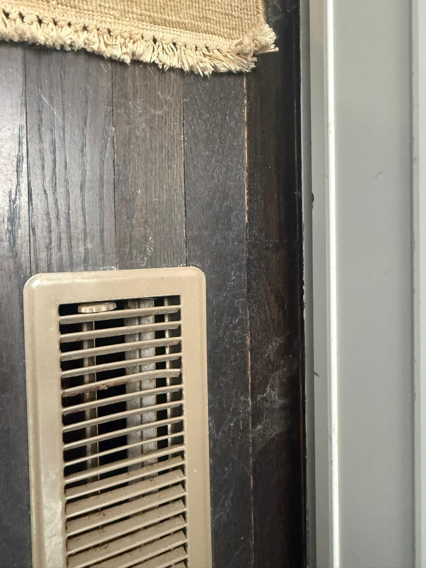 Beige wall vent on dark wood wall beside a light gray surface.