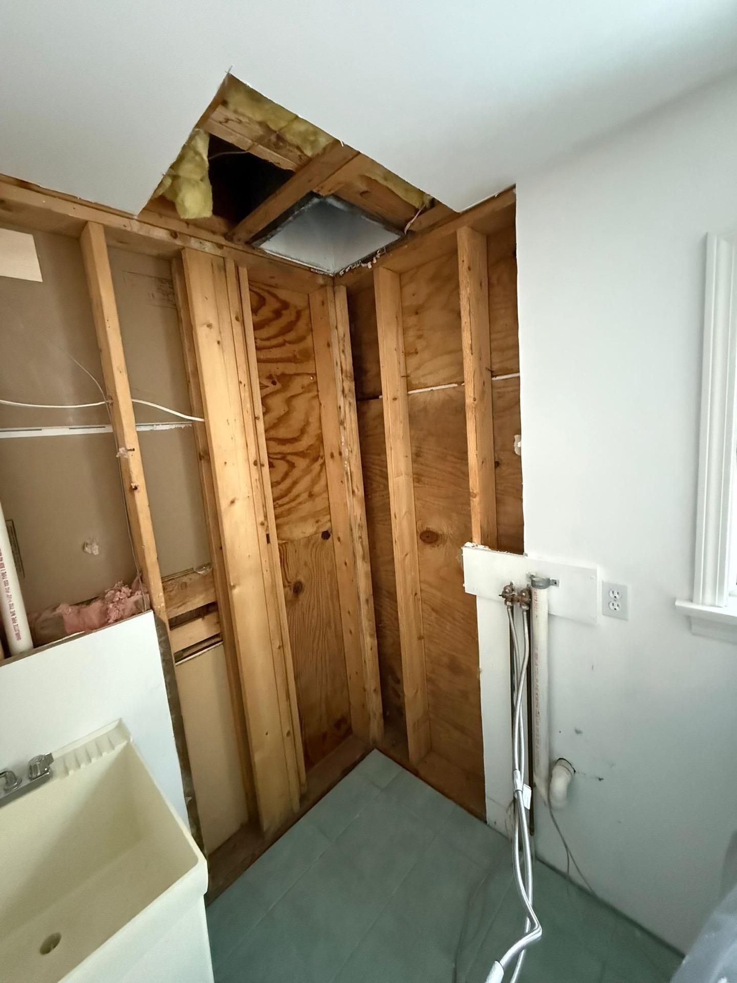 Bathroom under renovation with exposed wall studs and a partially open ceiling hatch.