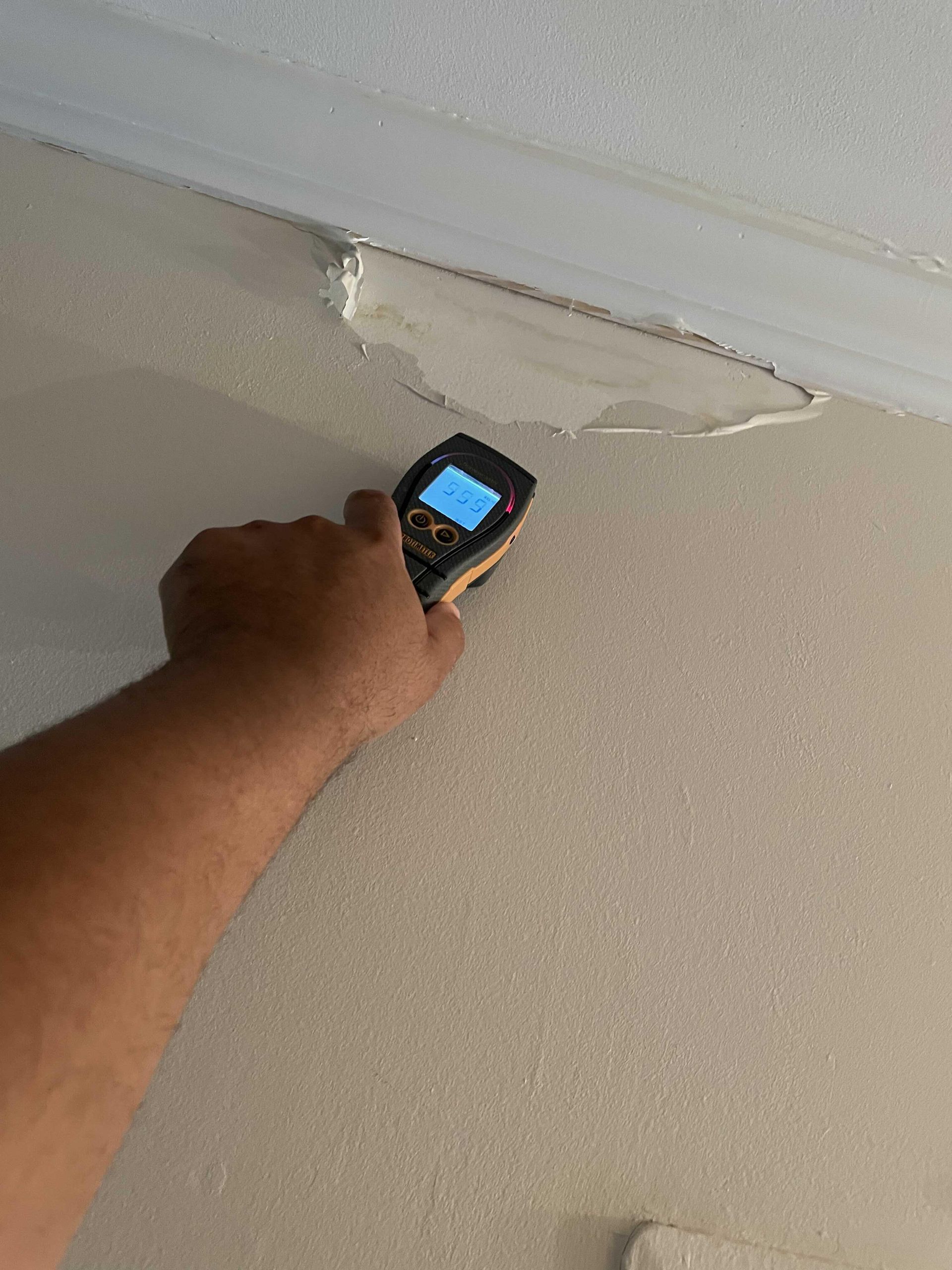 Hand holding a phone up to a damaged ceiling with peeling paint and a crack.