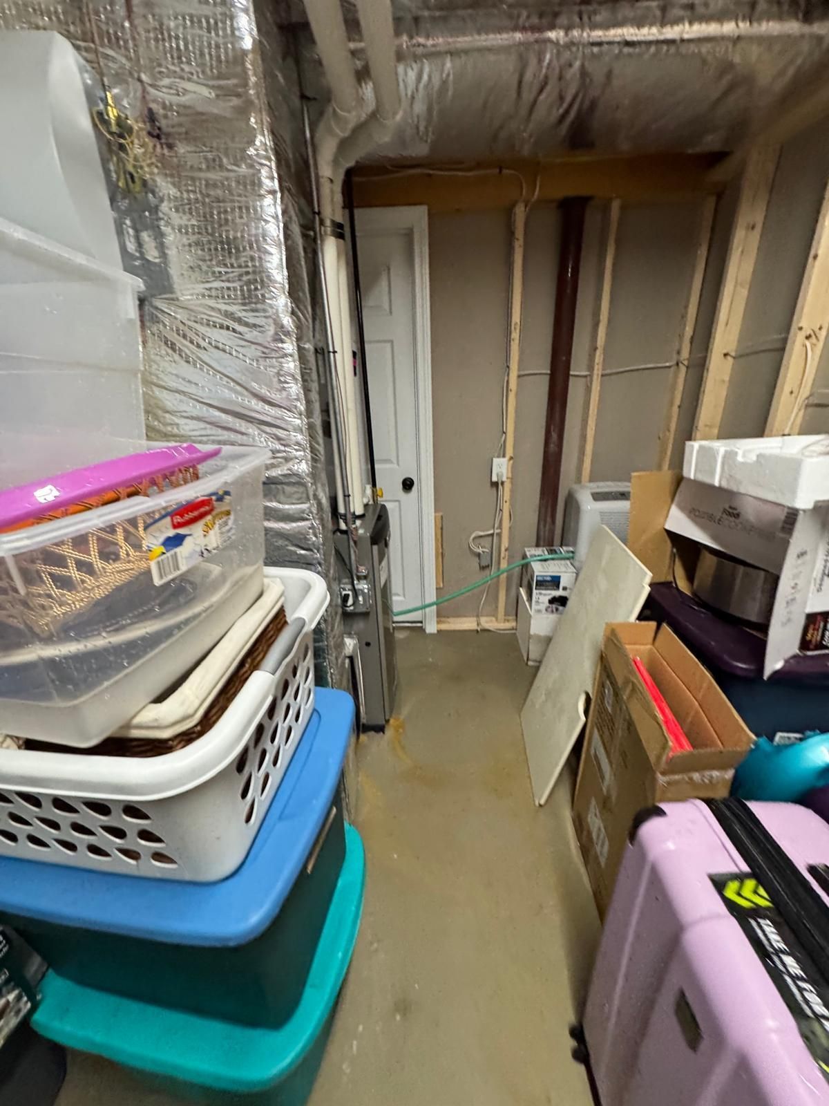Cluttered basement storage area with stacked bins, boxes, and wrapped items along unfinished walls