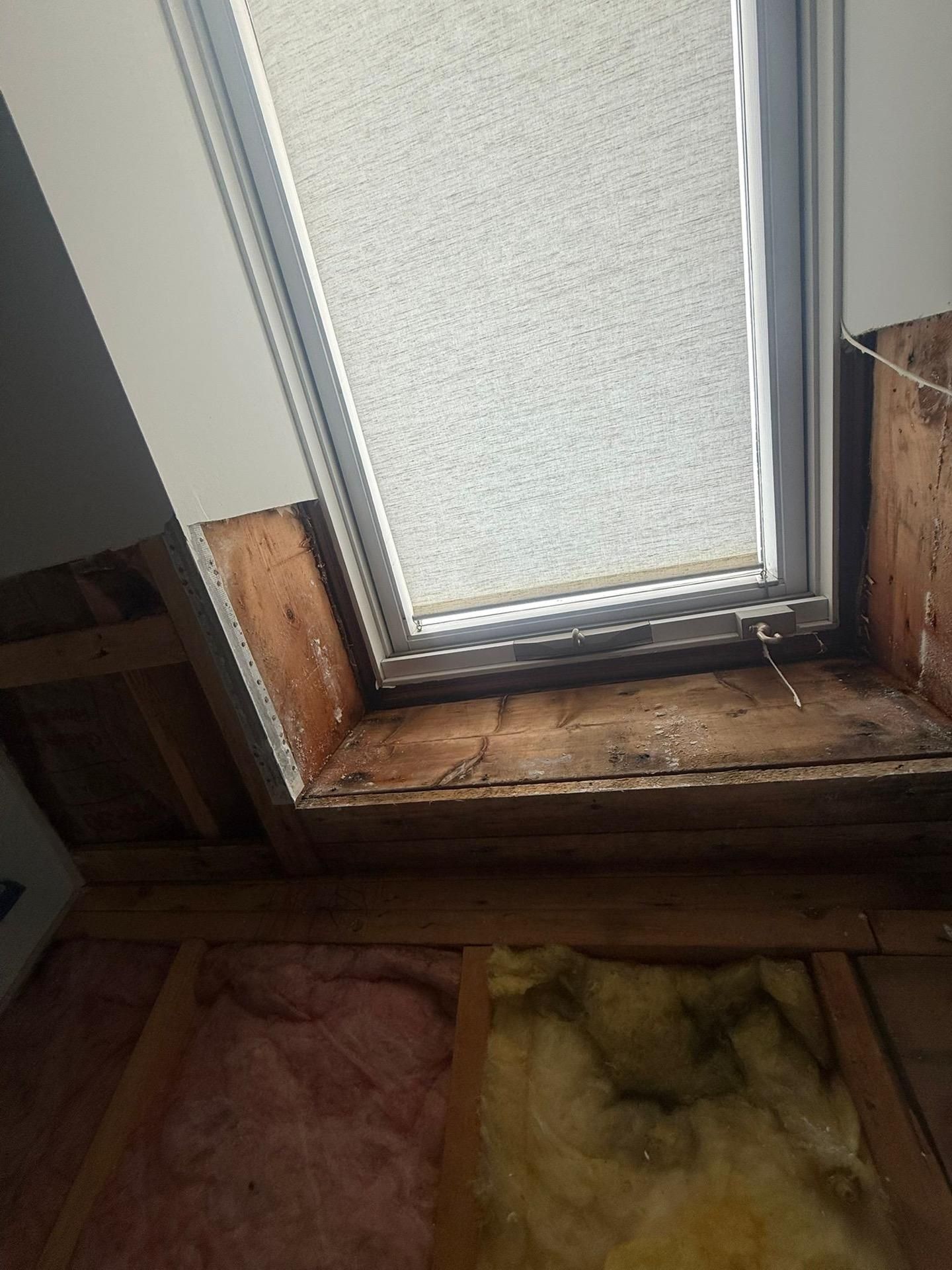 Close-up of a frosted window with wooden sill and exposed insulation below.