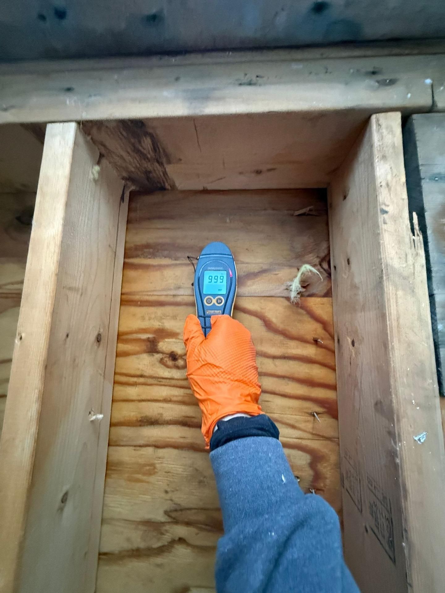 Person’s boot on plywood inside a wooden crawlspace, near an opening at the top.