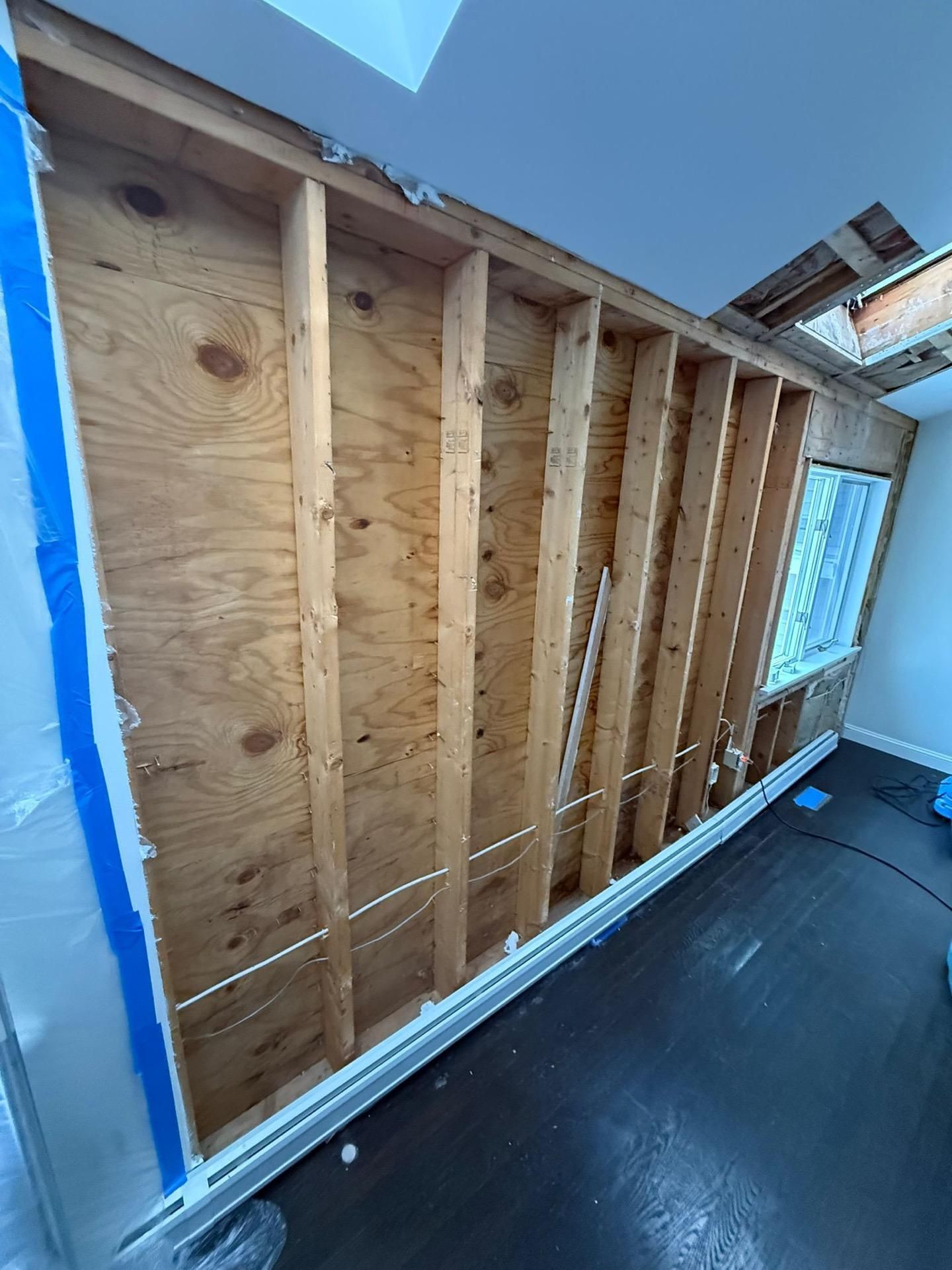 Interior wall framing with exposed wooden studs and plywood sheathing in a room under renovation