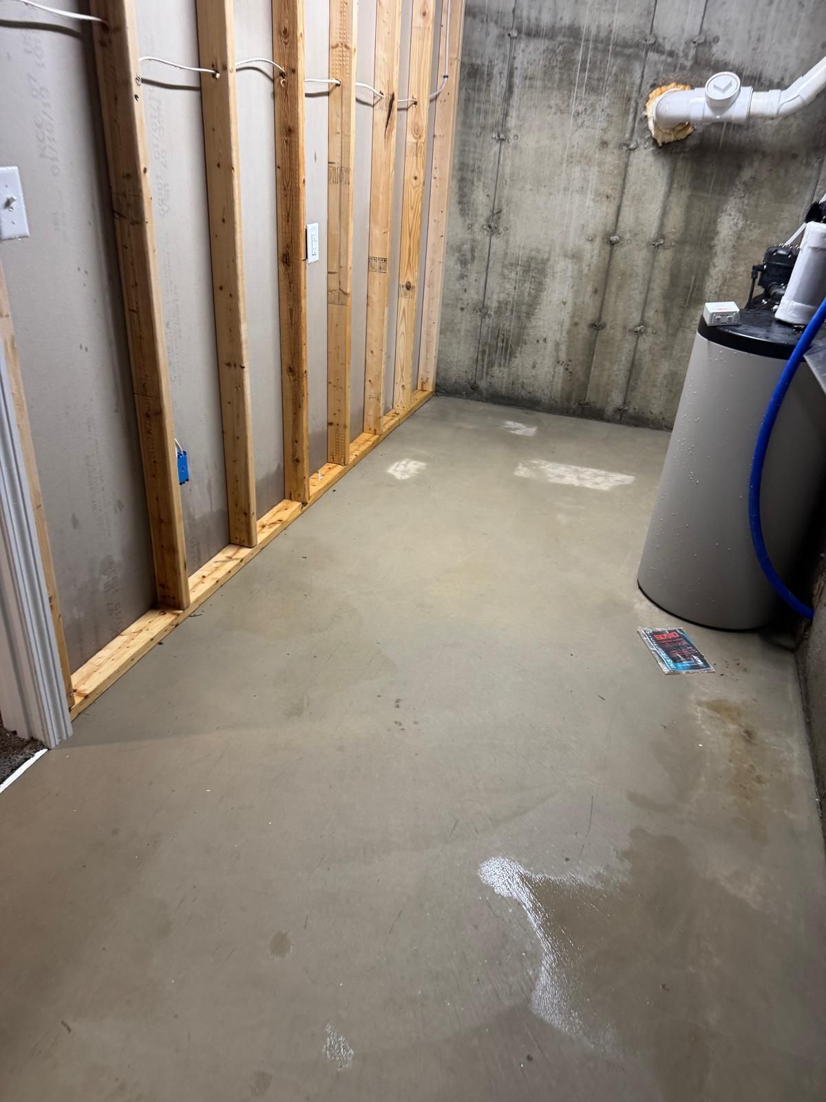 Unfinished basement utility room with concrete floor, exposed framing, and water softener tank.