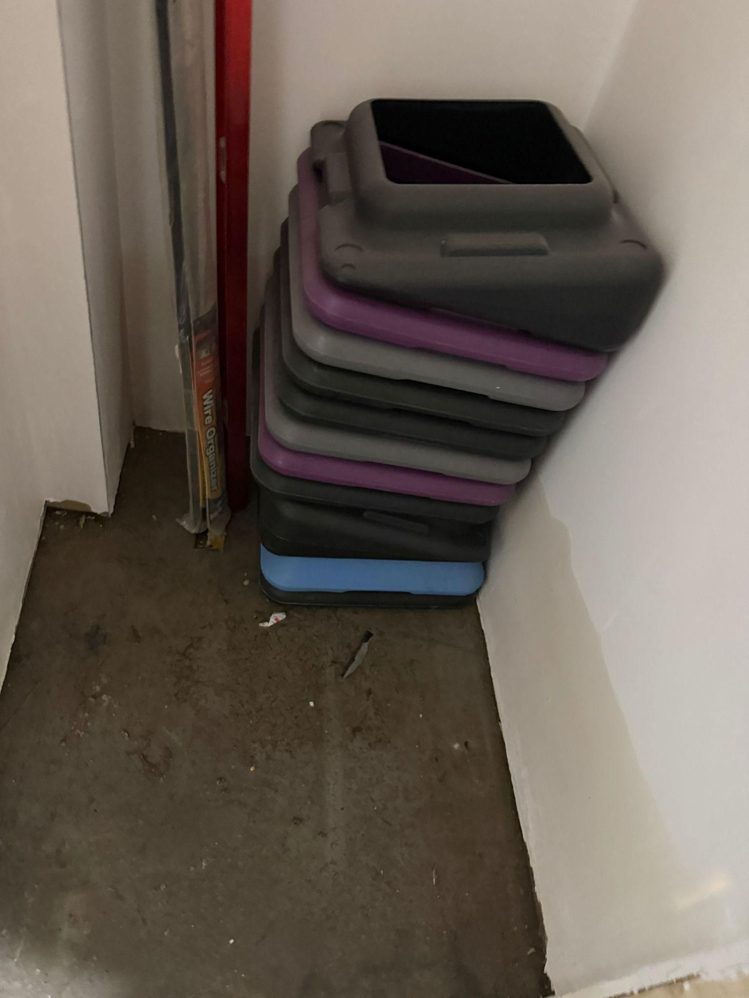 Stack of colorful storage bins beside a wall in a narrow hallway, with one open gray bin on top.