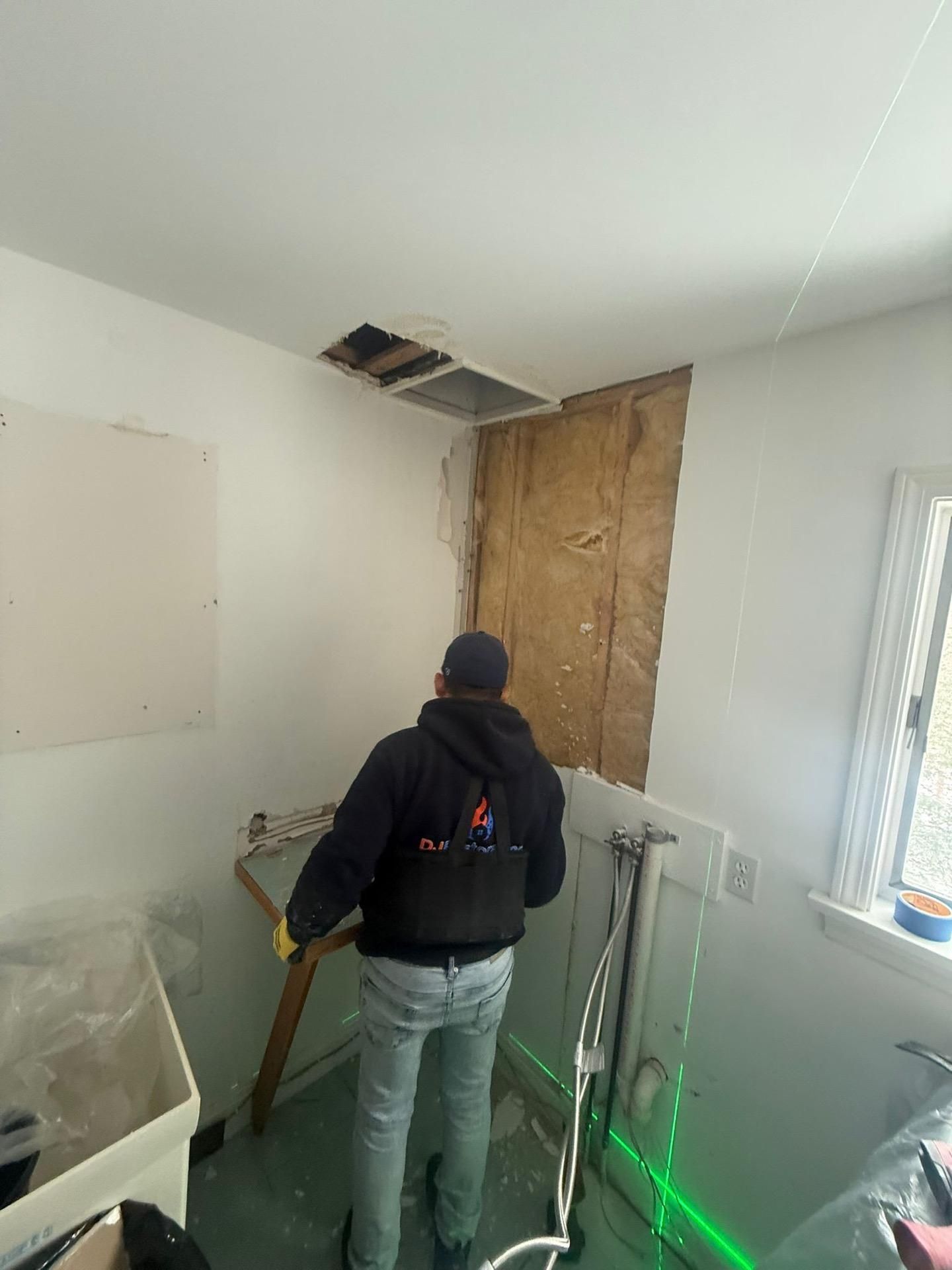 Person standing in a small room with exposed wall repair and tools, facing a boarded-up wall opening