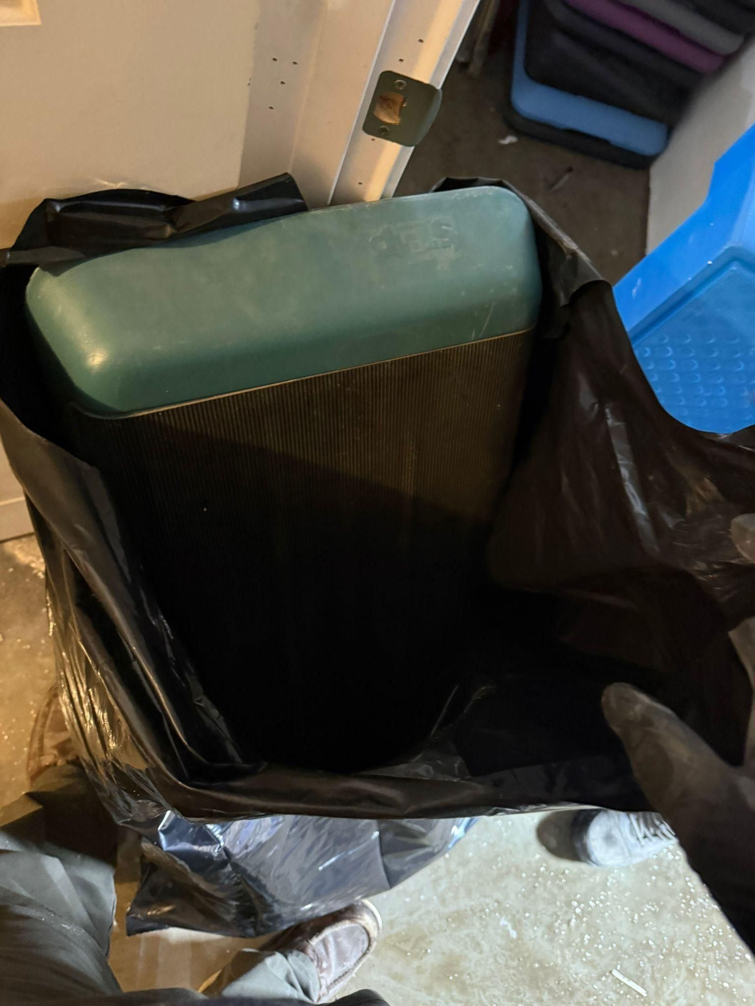 Open trash bin with black liner and green lid in a storage area