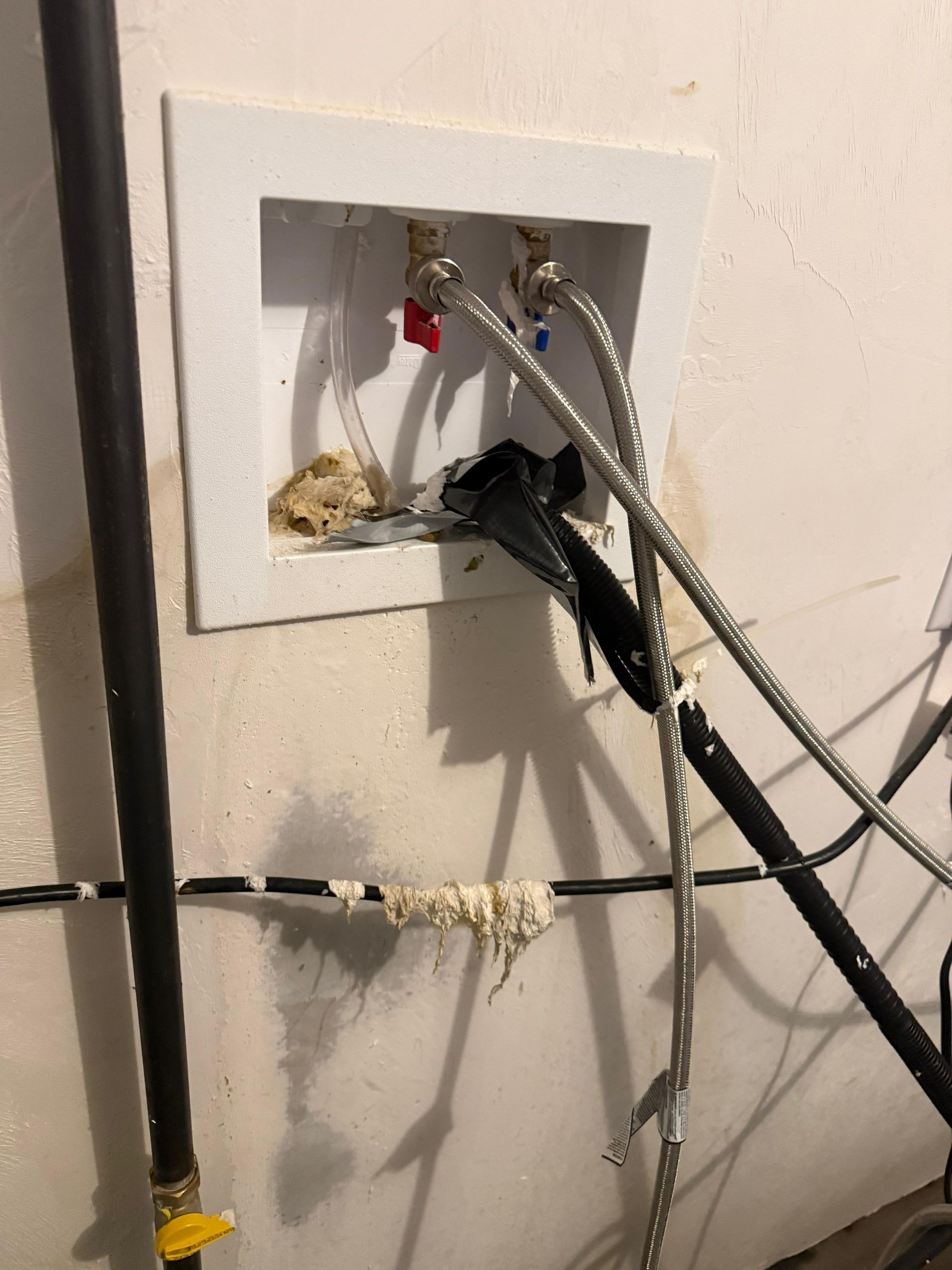 Wall outlet plate with multiple cables and plugs protruding from a rough wall opening