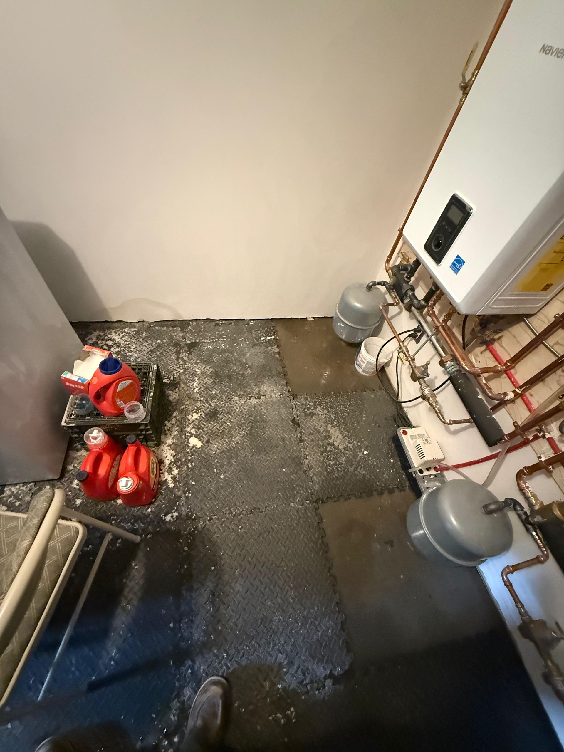 Small utility room with pipes, gas cylinders, and scattered debris on the floor.