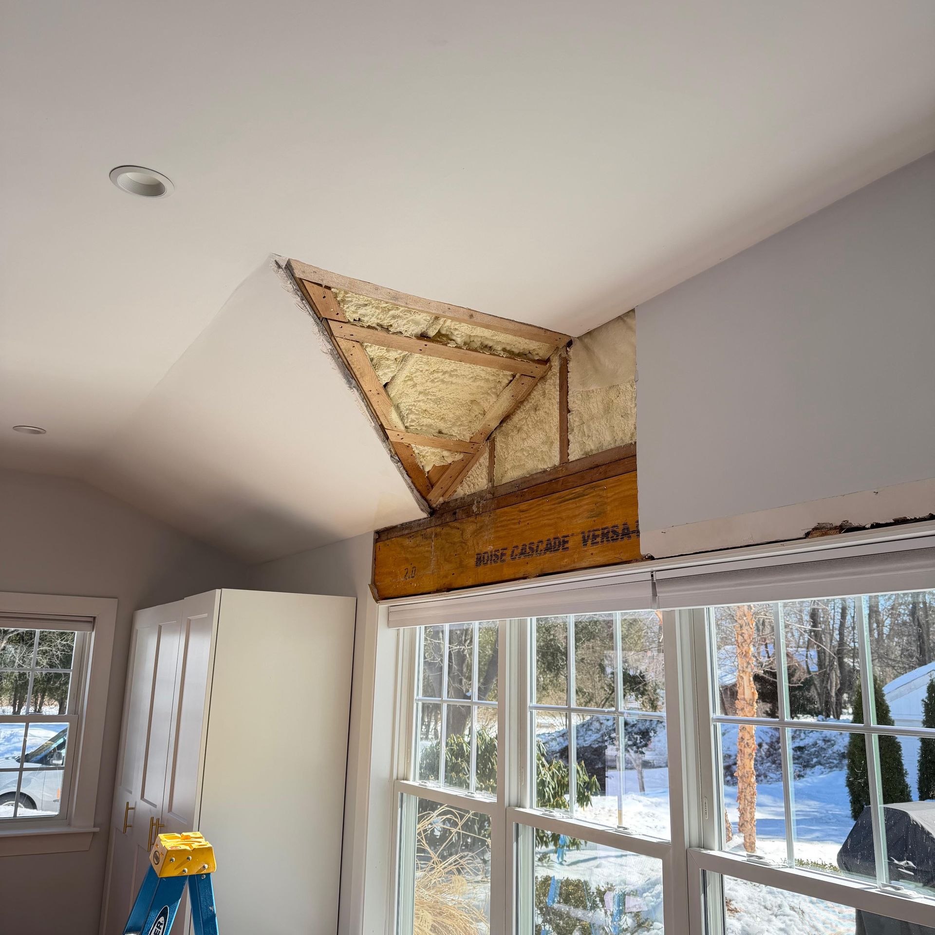 Interior room under renovation with open ceiling above a window and exposed insulation, drywall, and wood framing.