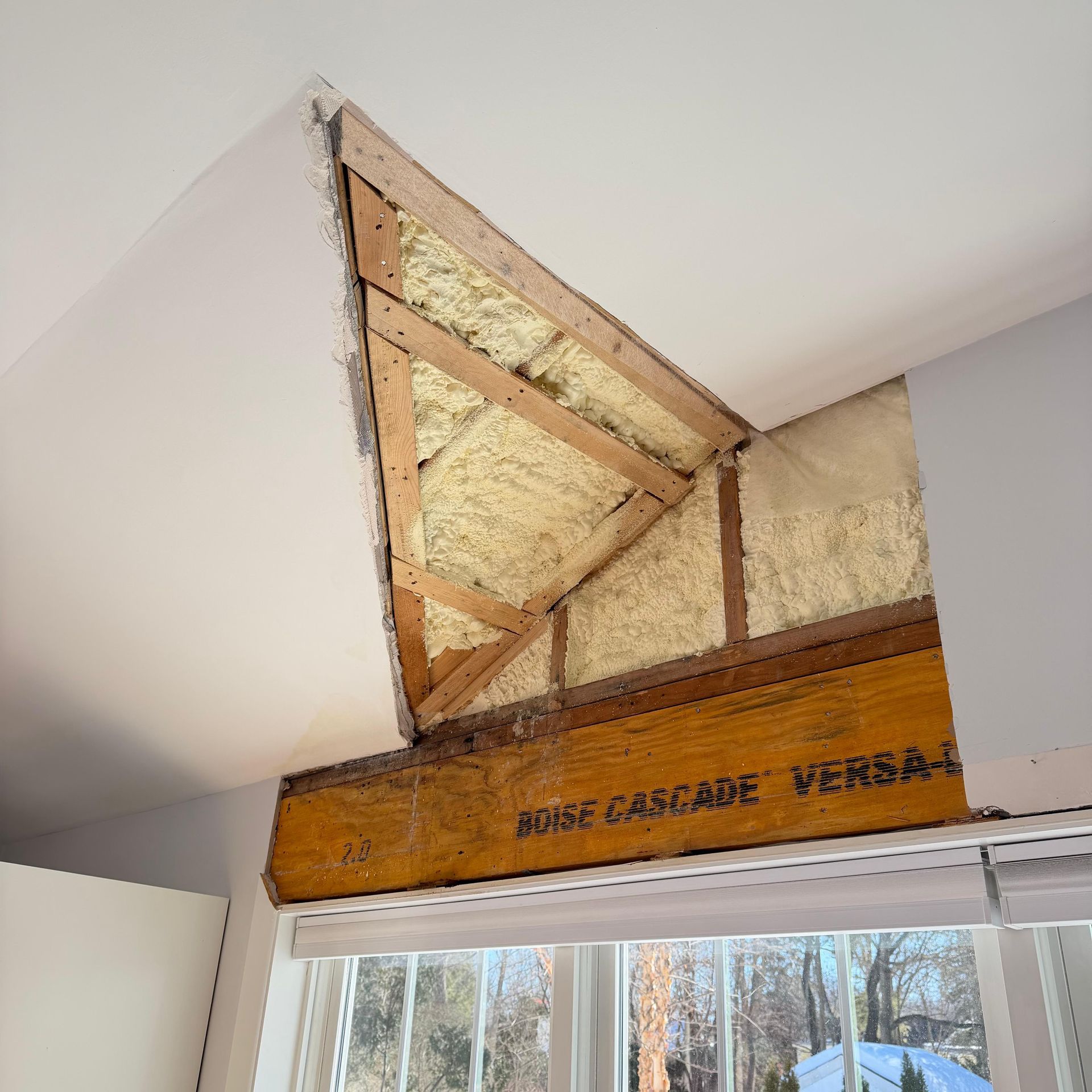 Partially open attic access above a window, showing exposed insulation and wood framing