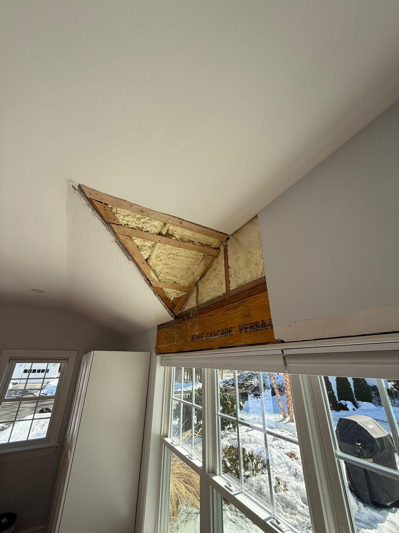 Tattered wall art hanging near a ceiling corner above windows in a bright room