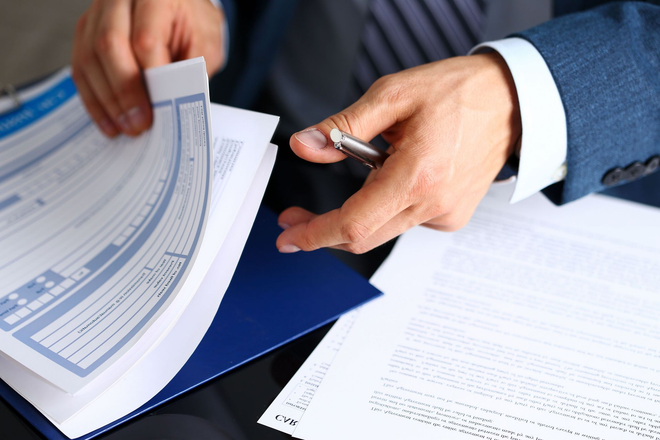 Hands reviewing paperwork with a pen and blue folder on a desk