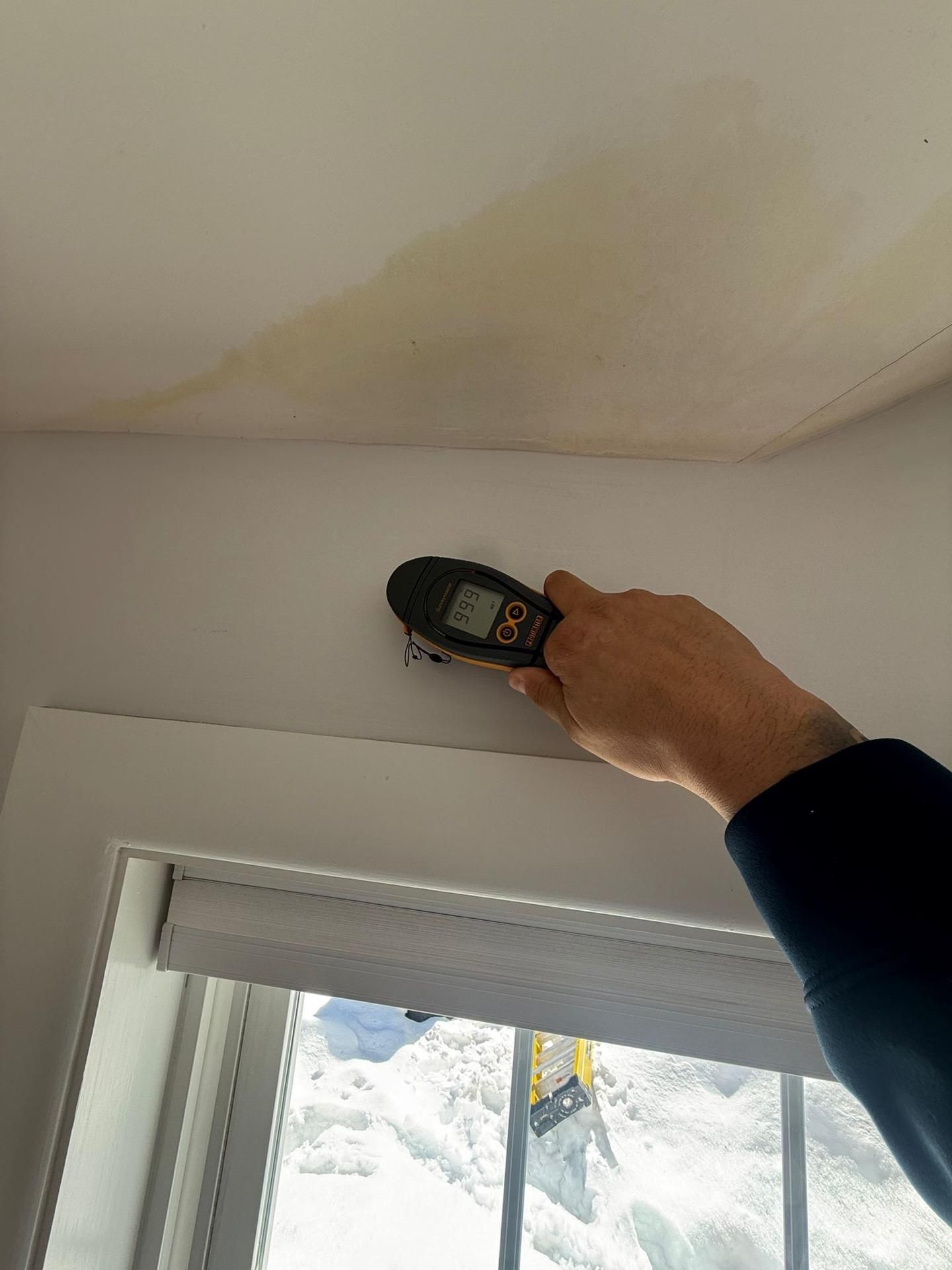 Handheld moisture meter checking a stained ceiling above a window