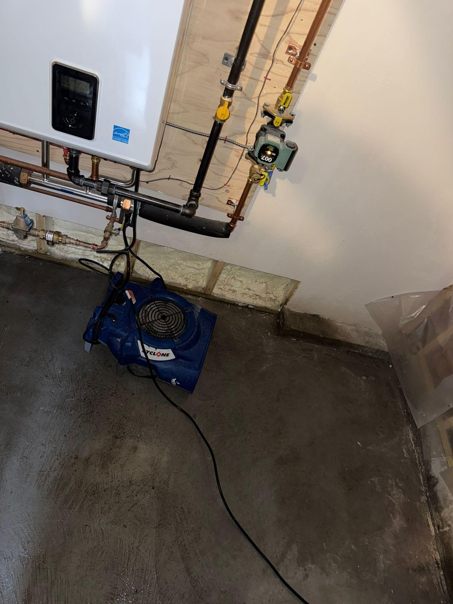 Utility room corner with electrical pipes, wall fixtures, and a blue bag on the concrete floor.