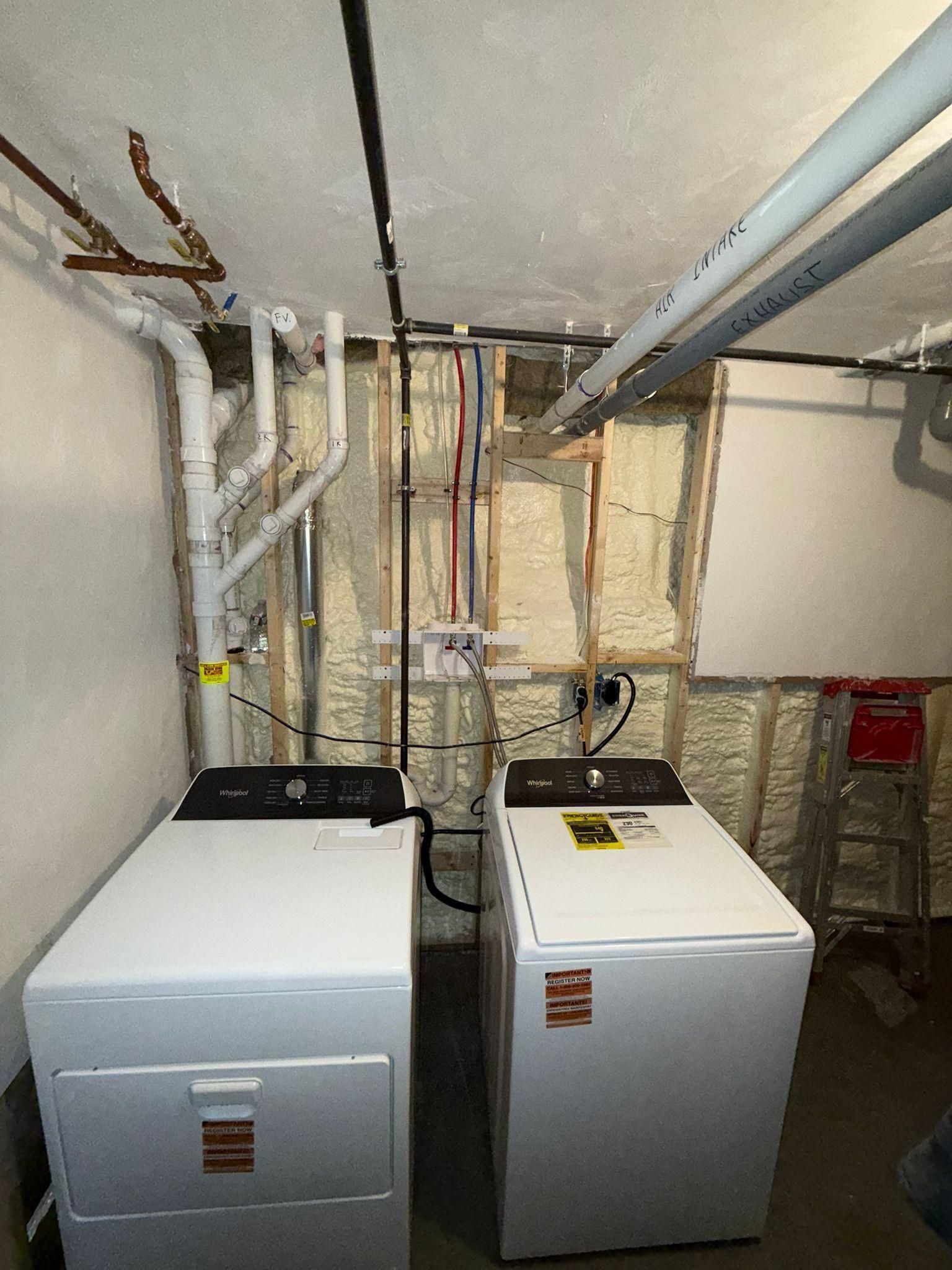 Basement utility room with two washing machines and exposed pipes and ductwork overhead