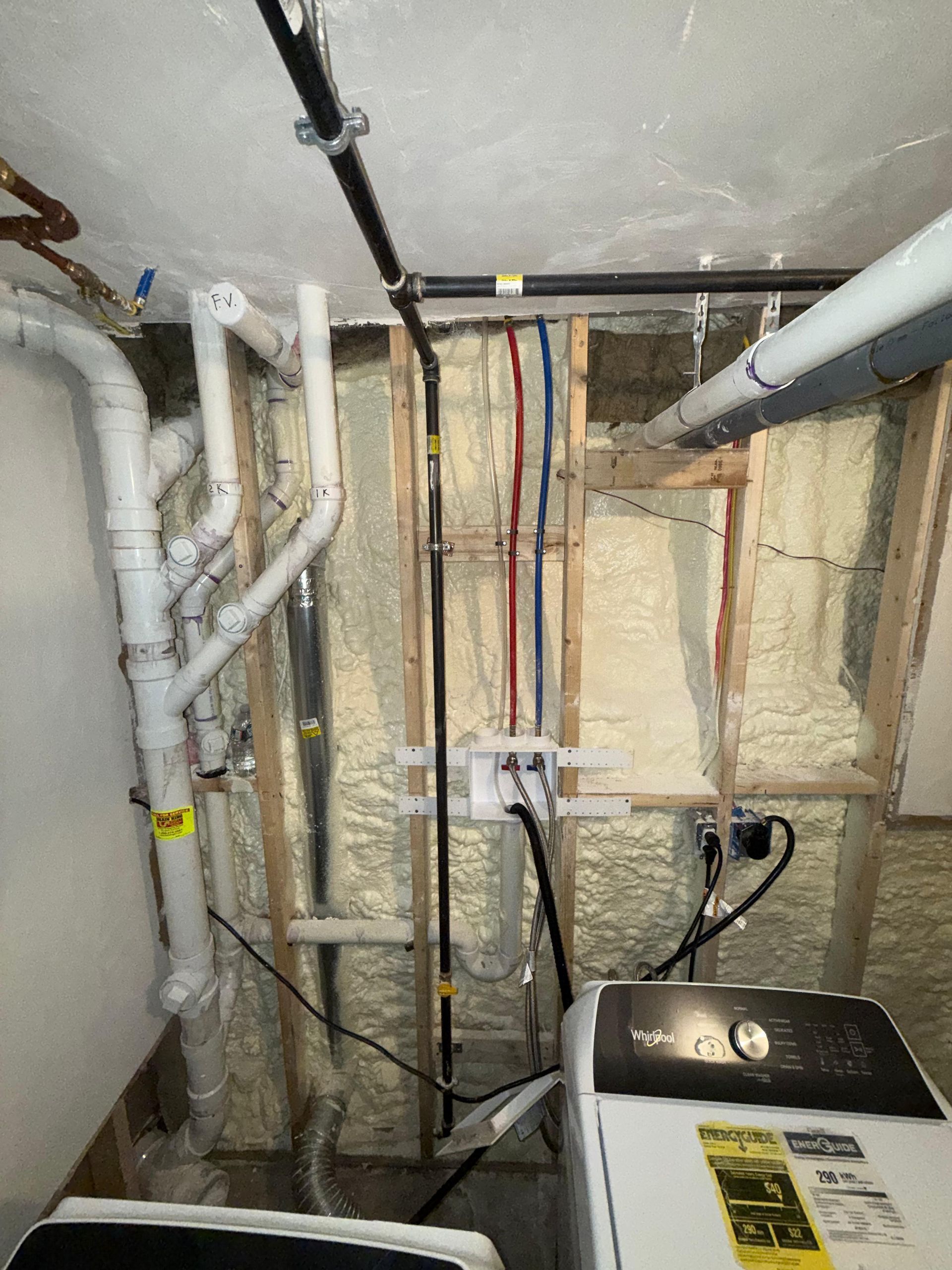 Basement utility area with exposed pipes, wiring, insulation, and a furnace or water heater.