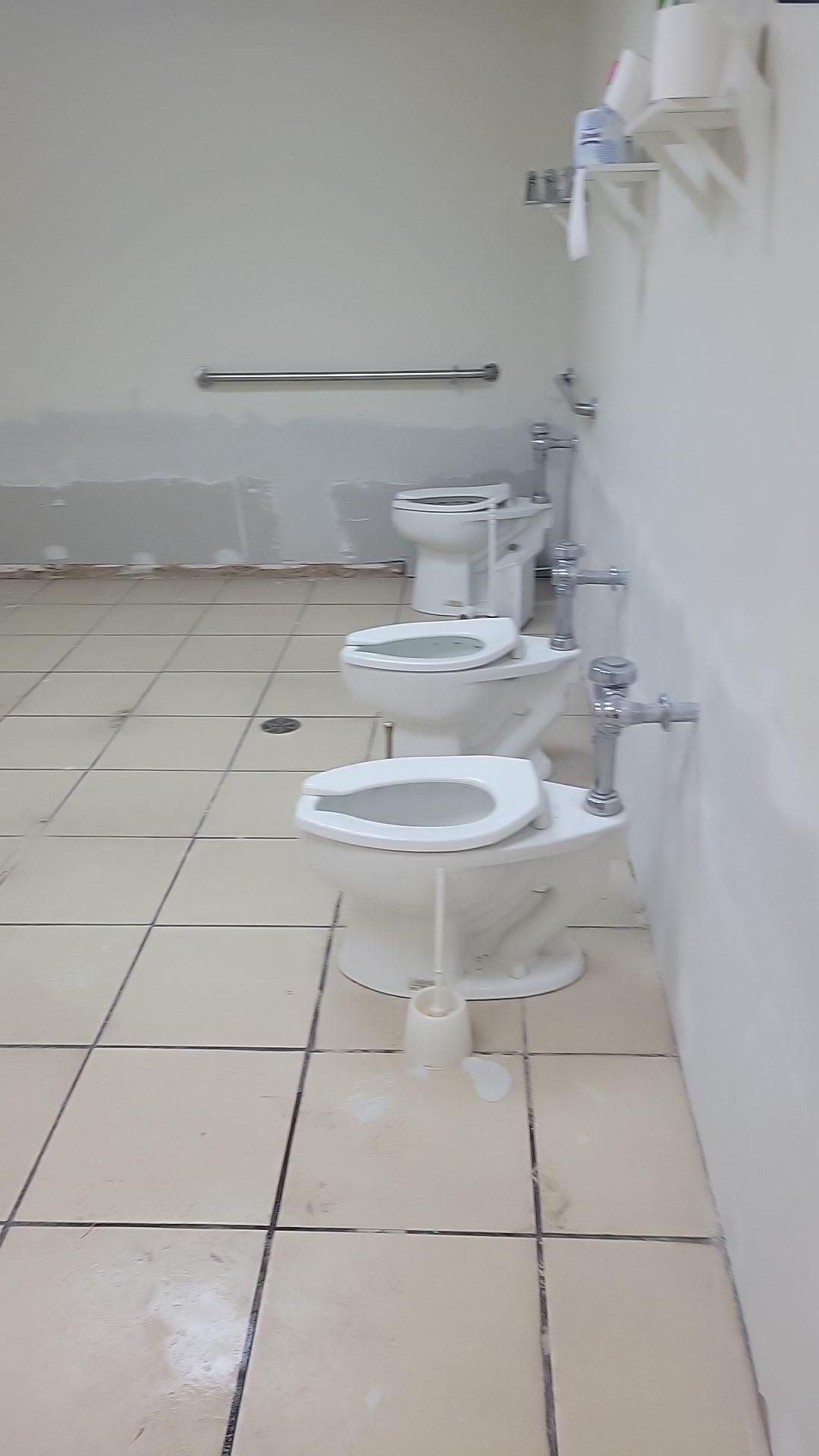 Public restroom with three wall-mounted toilets and white tiled floor.