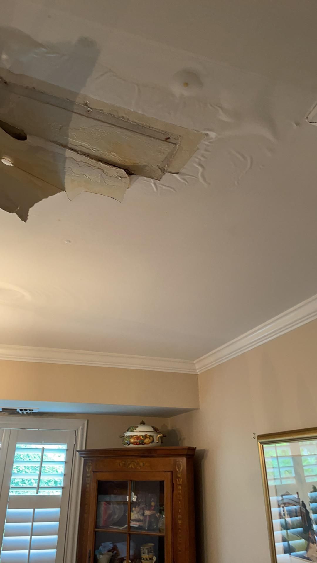 Ceiling water damage with peeling paint above a room with windows and a wooden cabinet