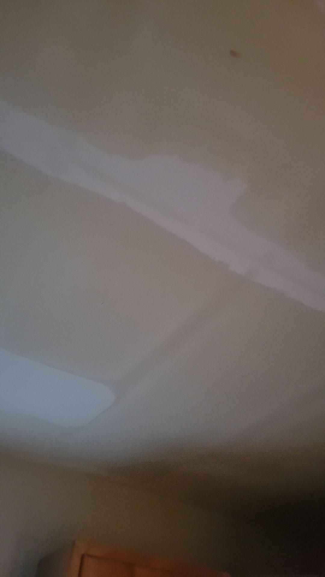 Close-up of a beige wall with a white diagonal strip and a small blue patch near the bottom left.