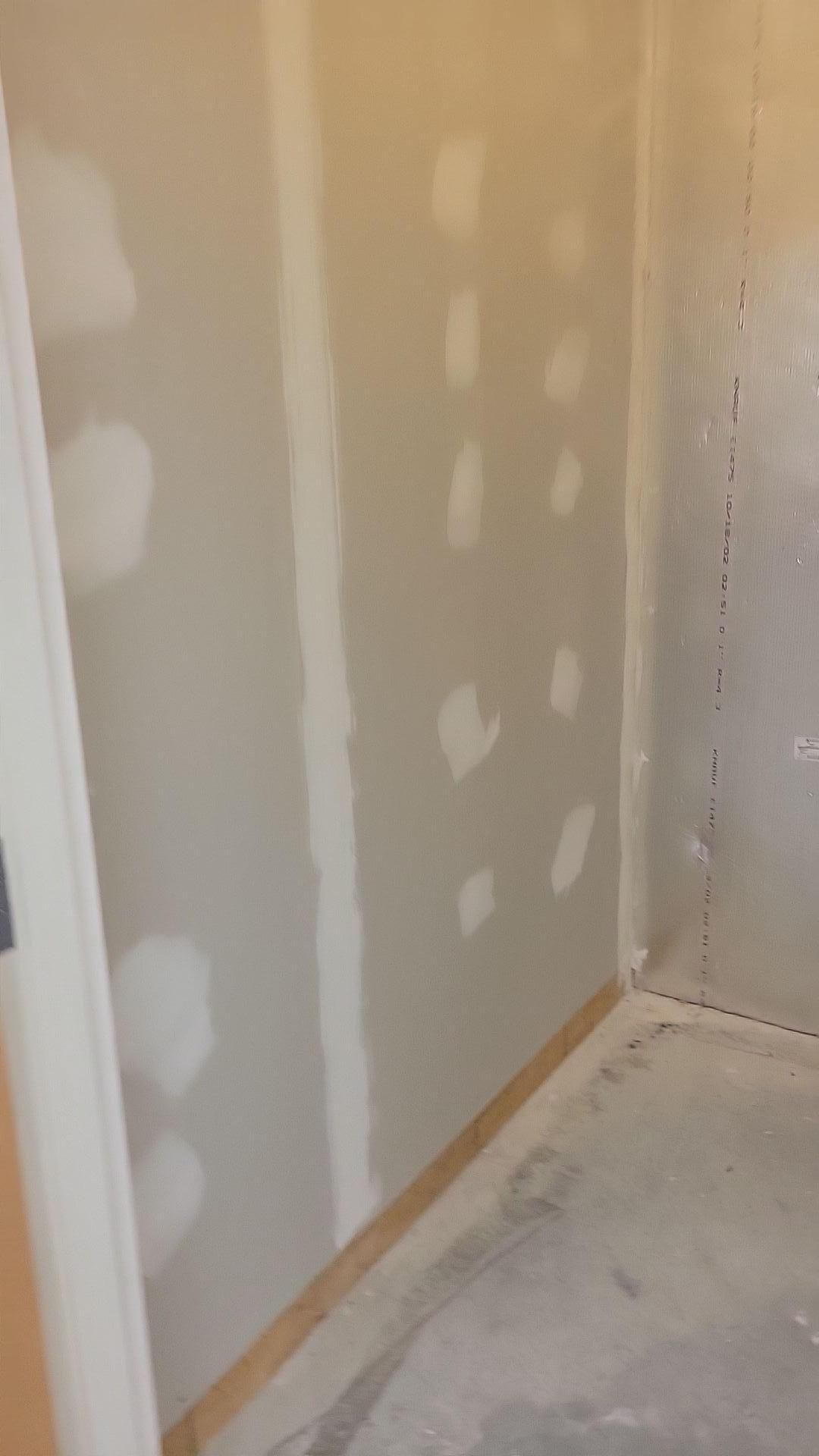 Partially finished drywall corner with white joint compound patches on beige walls and a dusty floor