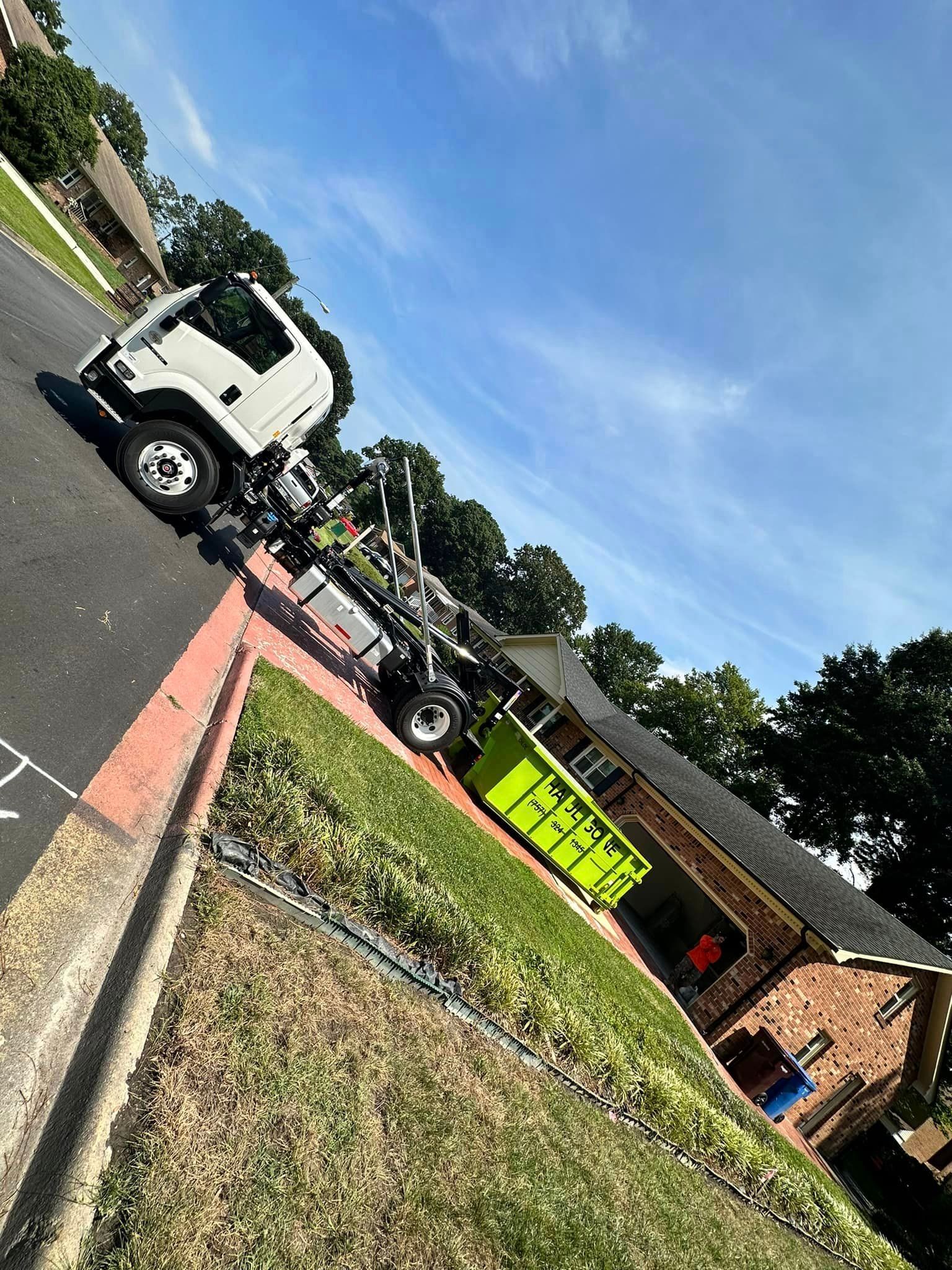 a green dumpster is parked in front of a house on the side of the road