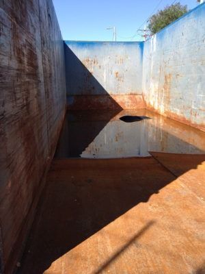 Inside of a large, rusty metal container filled with water. Sunlight casts a shadow across the interior.