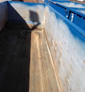 Blue dumpster interior, showing weathered metal, with sunlight casting a shadow.
