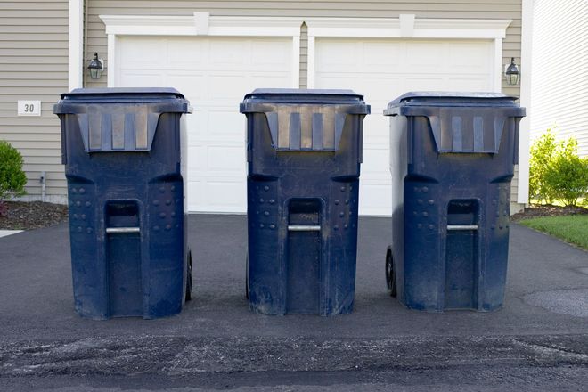 Three dark blue trash cans on a driveway in front of a garage.