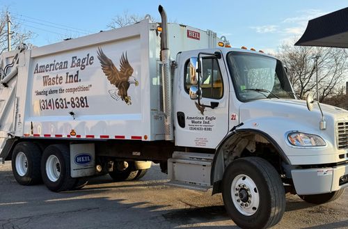 White American Eagle Waste Ind. garbage truck parked outside, logo with eagle graphic on the side.